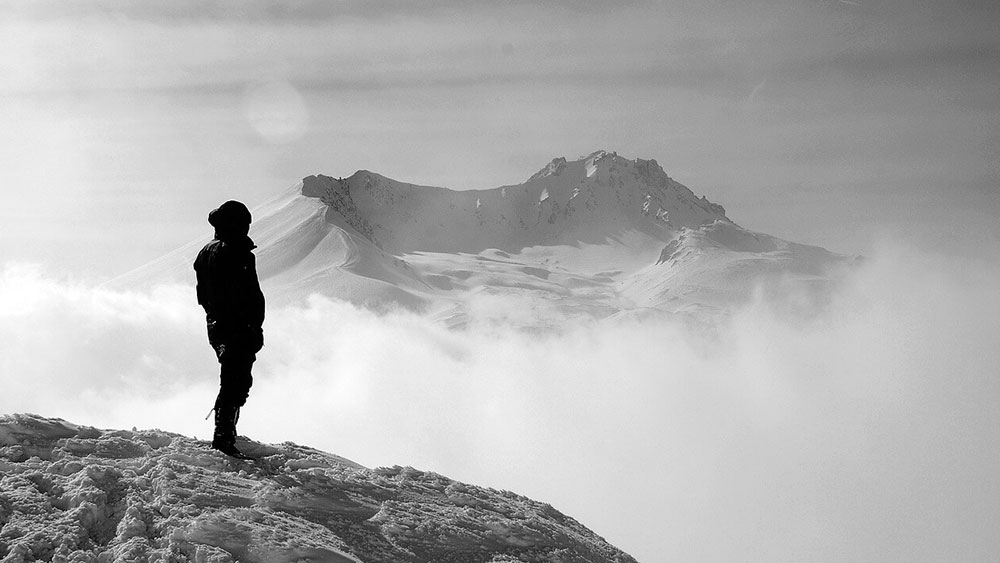 Човек на върха на заснежена планина наблюдава пайзажа