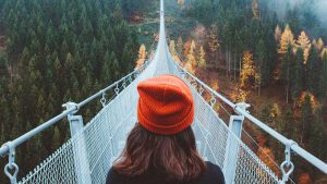 Момиче върху въжен мост съзерцава разкрилия се пейзаж