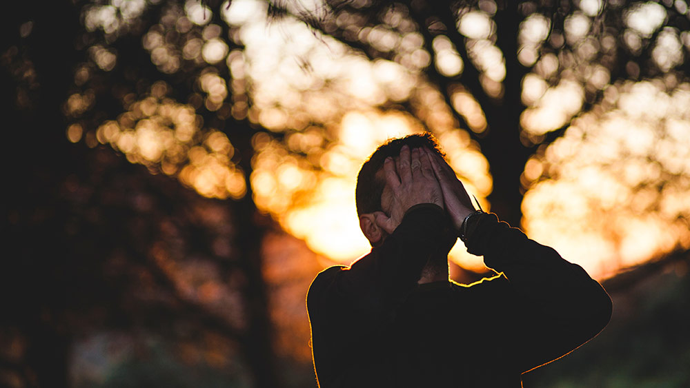 Depressed young man on sunset in background.