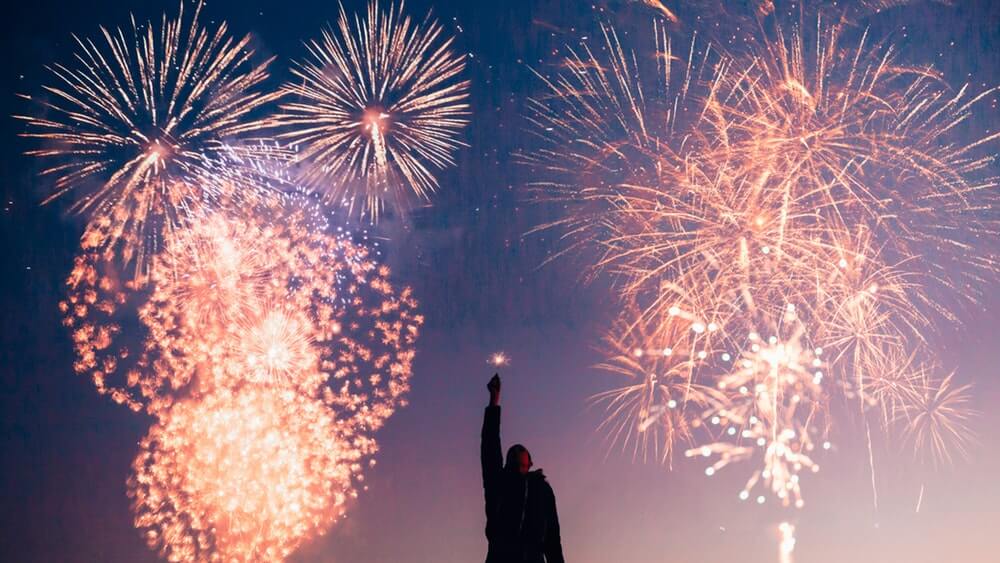 A man pointing towards fireworks-lit night sky.